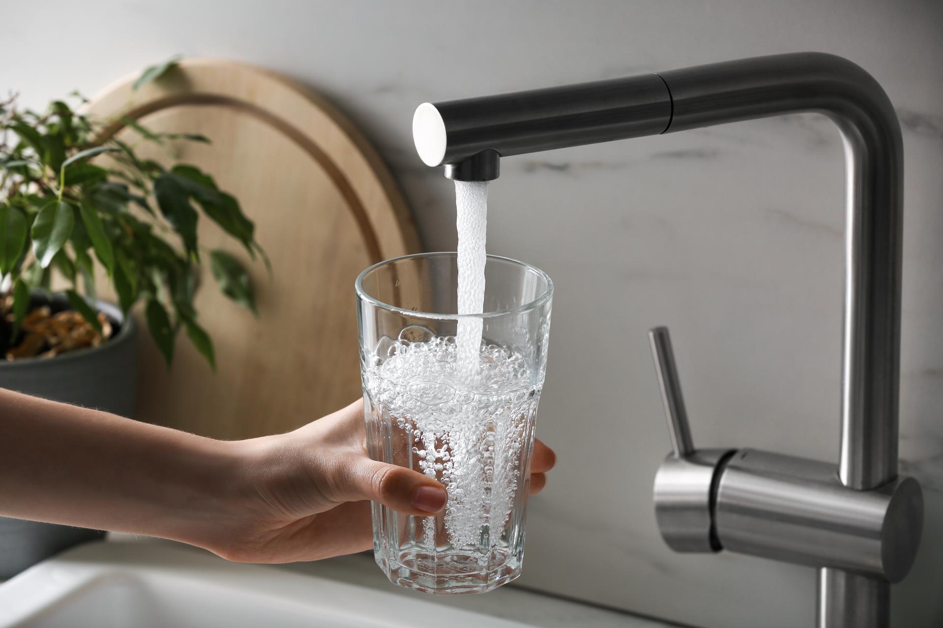 Woman filling glass with tap water from faucet in kitchen, closeup