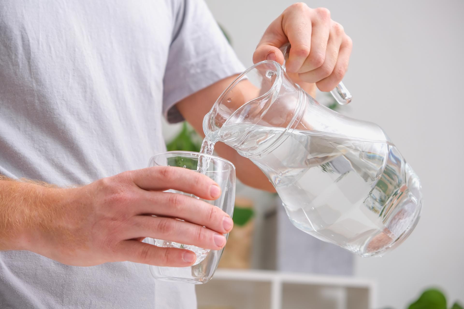 Man pours cold water into glass. Close-up of male hands pouring water from a jug into glass tumbler.